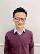 A man in a sweater and glasses smiles at the camera.