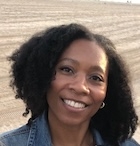 A woman with black hair in a jean jacket smiles at the camera.