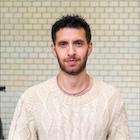 A man in a white sweater looks at the camera.