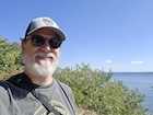 a man with a beard and hat in front of a blue sky.