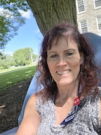 A woman in an SP red pin smiles in a blue Adirondack chair. 