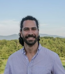 A man in a button up shirt in front of a mountain view. 