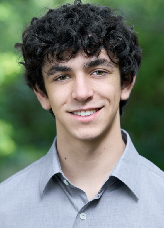 A man in a gray collared shirt smiles at the camera. 