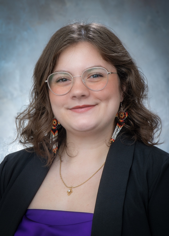A woman in a purple shirt and black jacket smiles at the camera. 