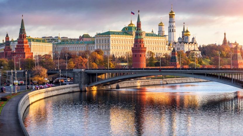 River running through city in Russia with buildings and bridge in background.