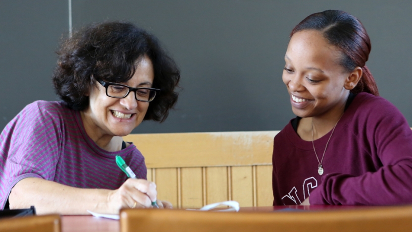 A Spanish language student and her professor work together sitting at a table.