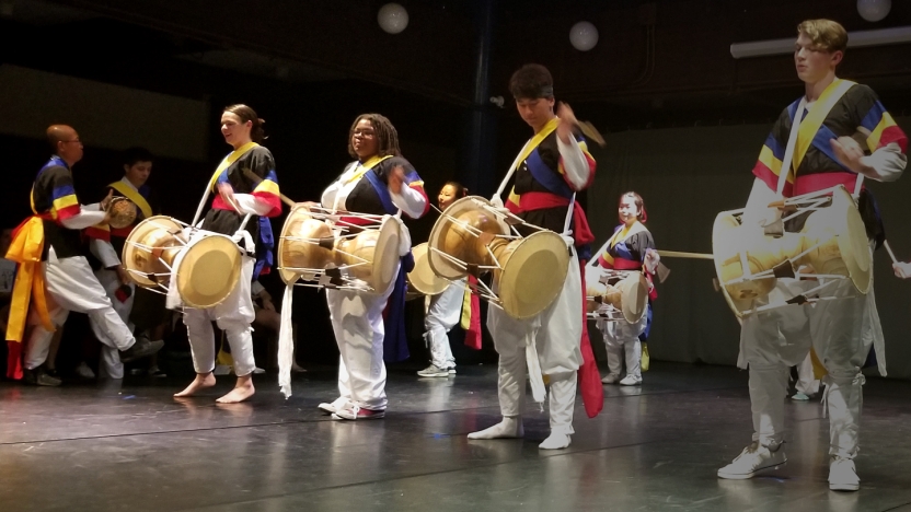 Students drum in performance on stage.