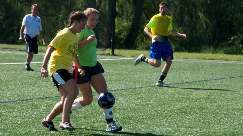 Three spanish language school students playing soccer with referee in background.