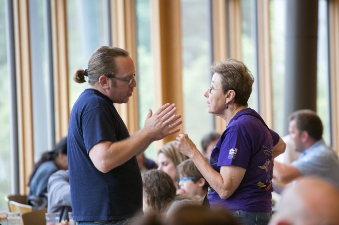 Two Hebrew Lifelong Learners have a discussion in crowded dining hall.