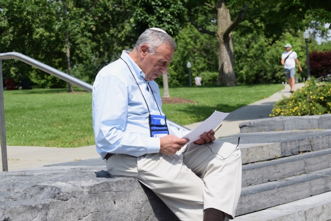 Male Hebrew Lifelong Learner student sitting on steps outside of library, reading.