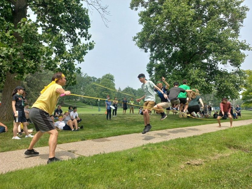 two men swing a long jump rope while another man jumps over it. 