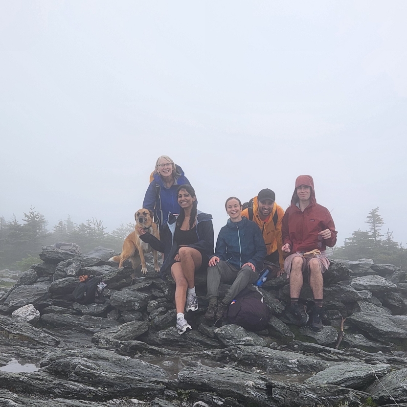 People pose at the top of a mountain with a dog, smiling. 