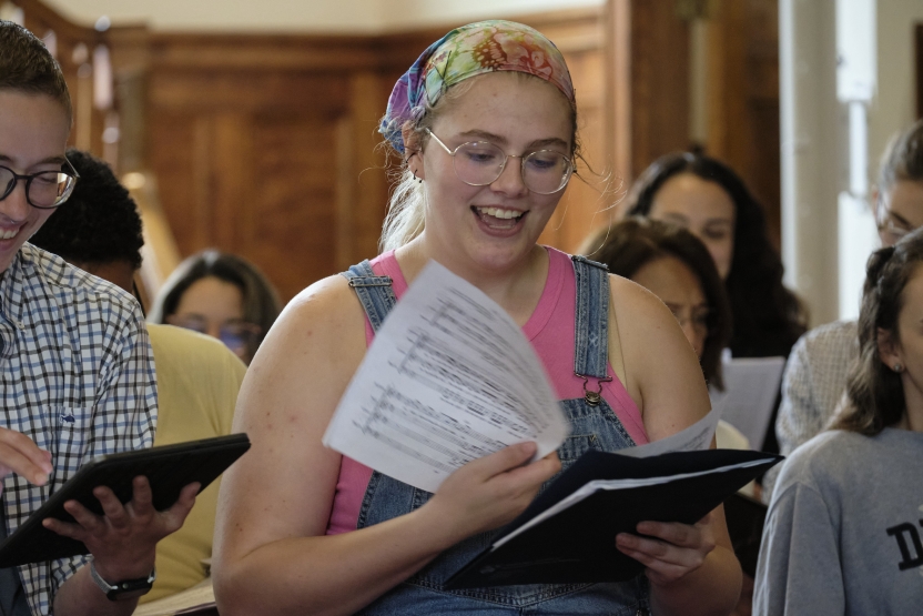 Woman smiles as she reads her sheet music. She stands in the crowd of a choir.