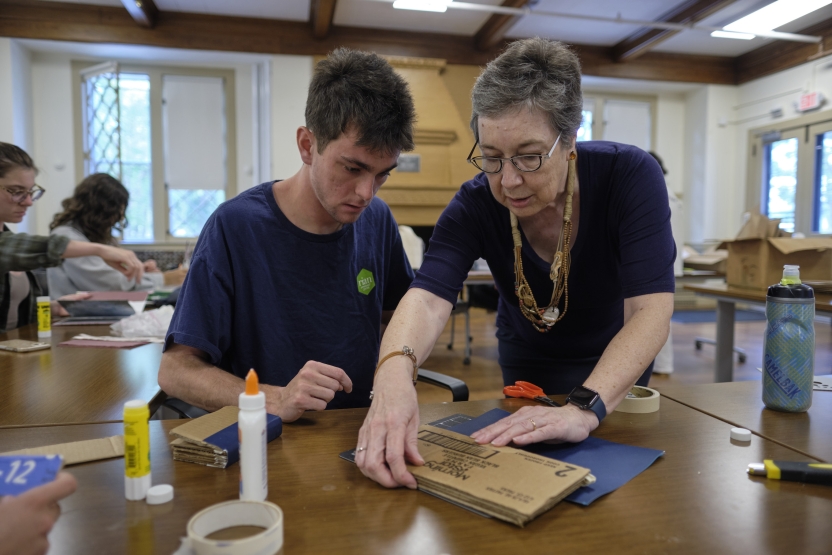 A woman helps a young man place a piece of cardboard to finish binding his book. 