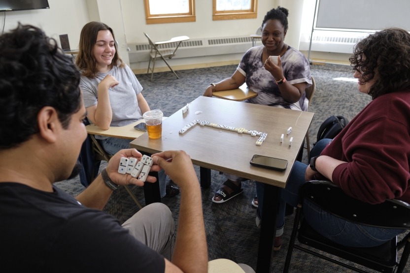 A group of young people smile as they hold their dominos in their hands around a table.