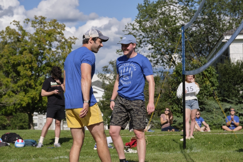 Two men pass each other happily, celebrating an outdoor volleyball play. 