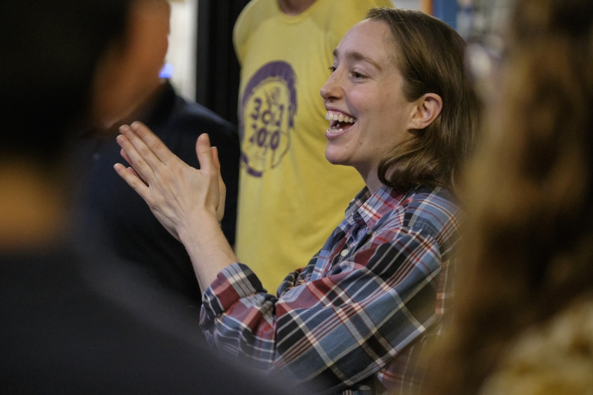 A woman claps and smiles, surrounded by a group. 