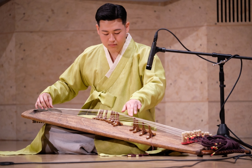 A musician plays traditional Korean music as he sits on a stage. 