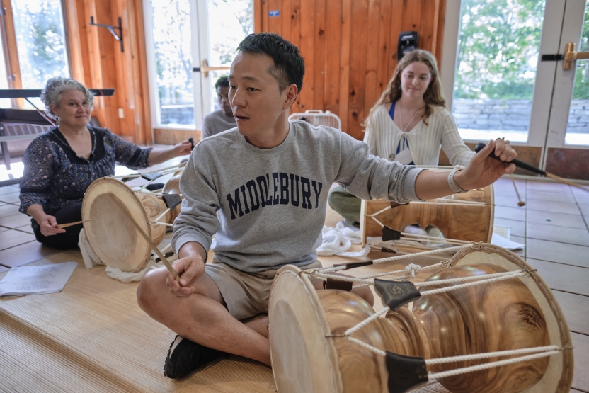 A teacher teaches students how to drum on a Korean drum. He sits in front of his students, leading them. 