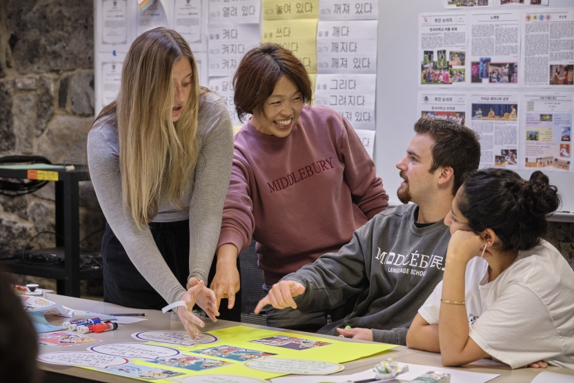 Students discuss their Korean comic strips with their teacher- the teacher smiles. 