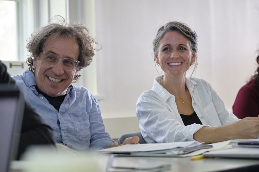 Two students sit side by side in class, smiling up at the teacher. 