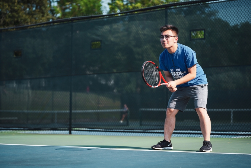 A student plays tennis on an outdoor court. 
