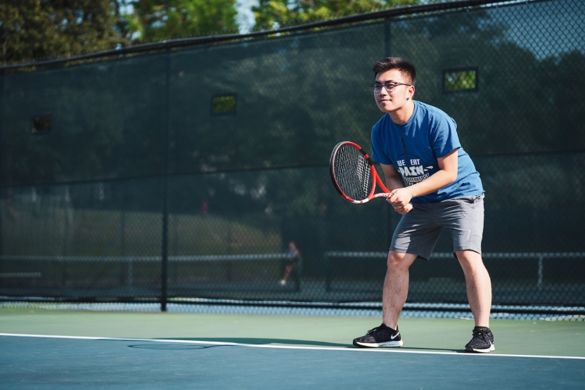 A student plays tennis on an outdoor court. 