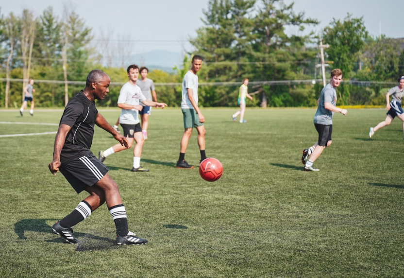 A group of men play soccer outside on a grass field. 