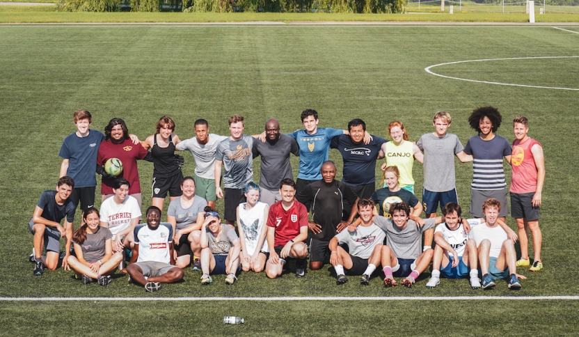 A group of students on a soccer team stands in a group, smiling. 