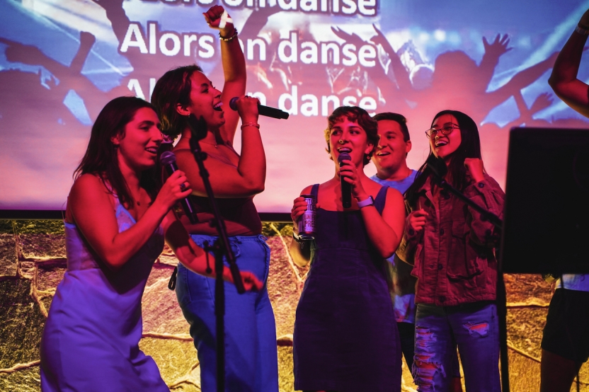 Students sing karaoke together in colored lights, smiling. 
