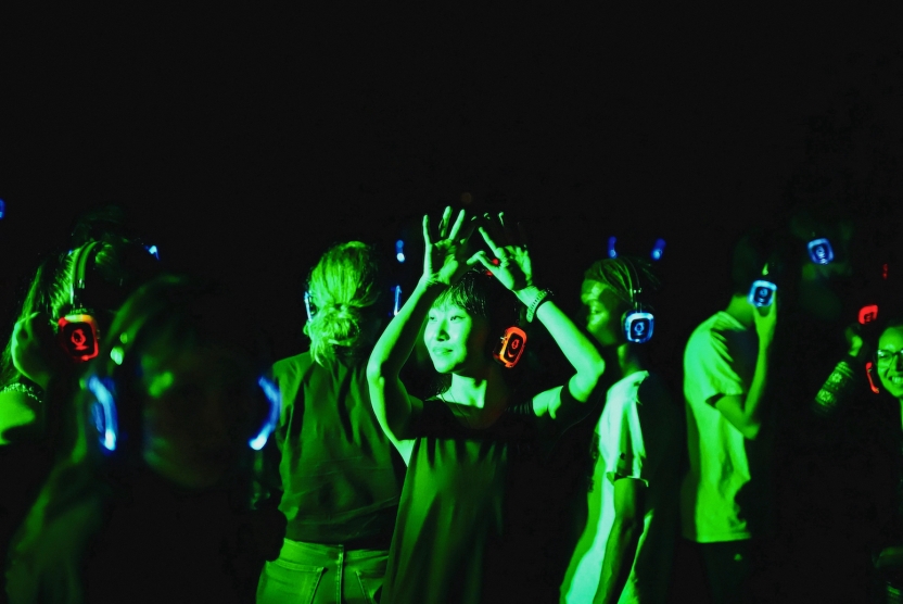 Students dance in green light with headphones on, a silent rave. 