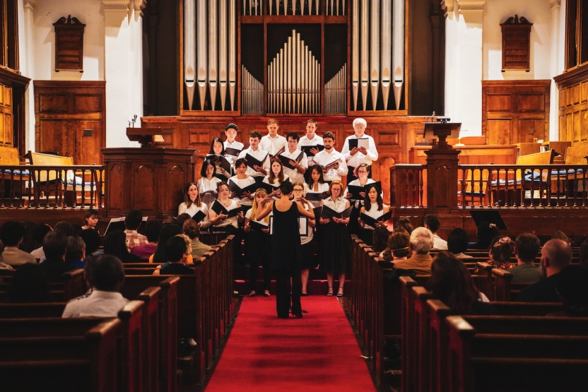 Students sing in a choir during the evening. A crowd watches. 