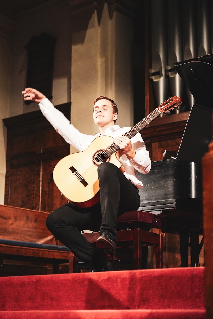 A student plays guitar, his arm raised in a flourish. 