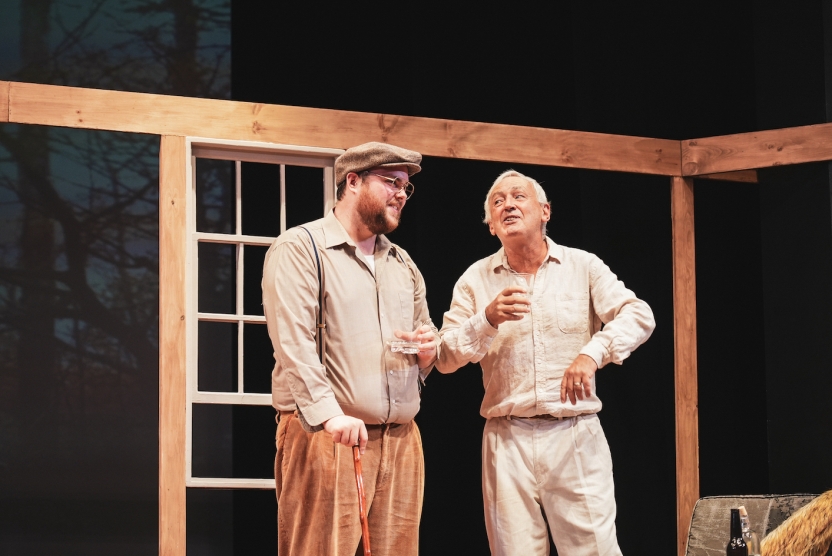 Two men, actors in a play look at each other smiling. 