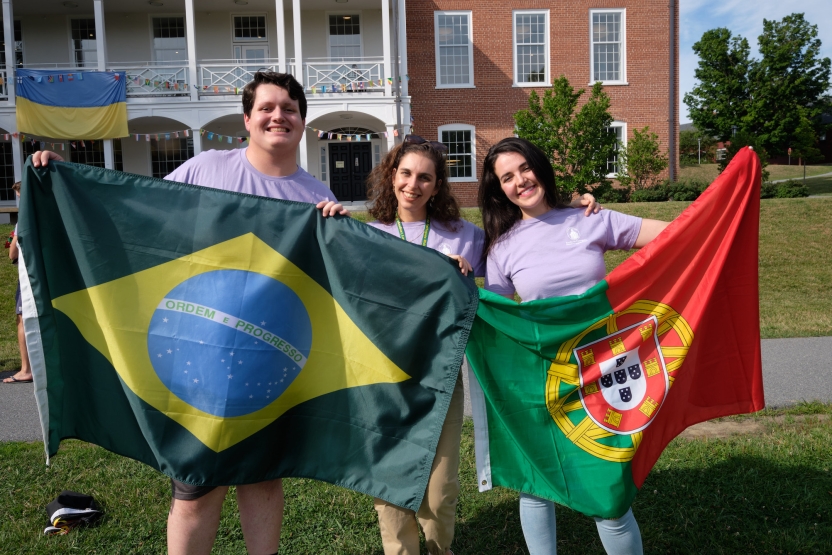 Students hold up flags from Portuguese speaking countries, smiling at the camera. 