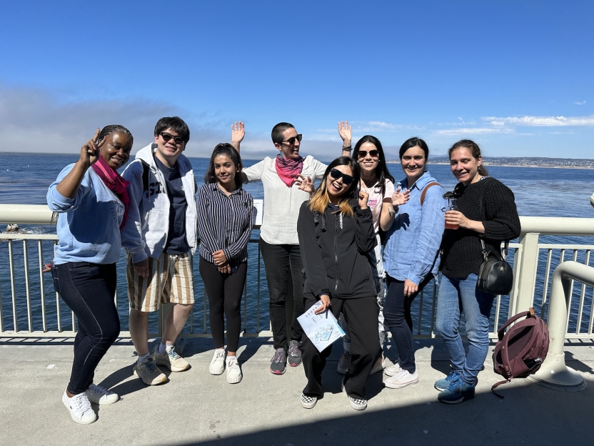 Students stand in front of the ocean, smiling at the camera in a large group.