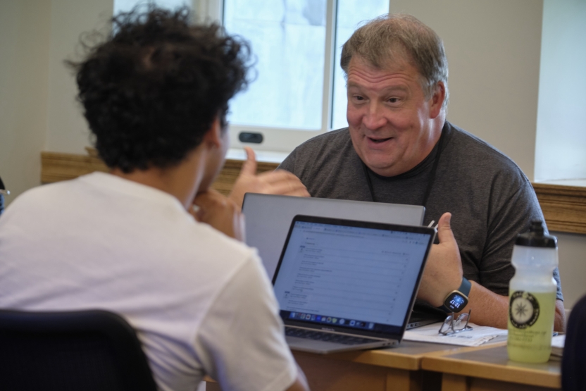 An older gentleman speaks with his hands across the desk from his peer.