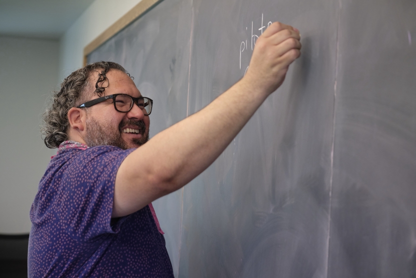 A man smiles as he writes in Spanish at the whiteboard. 