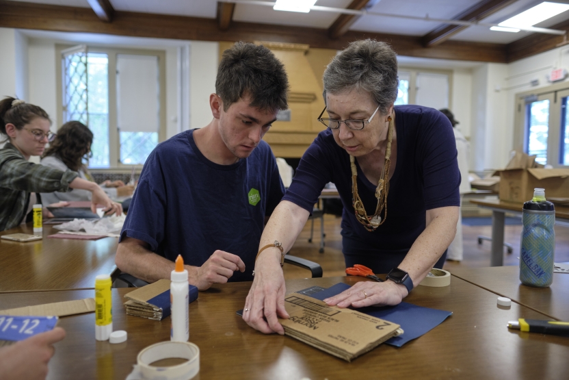 A woman shows a young man how to bind a book. 