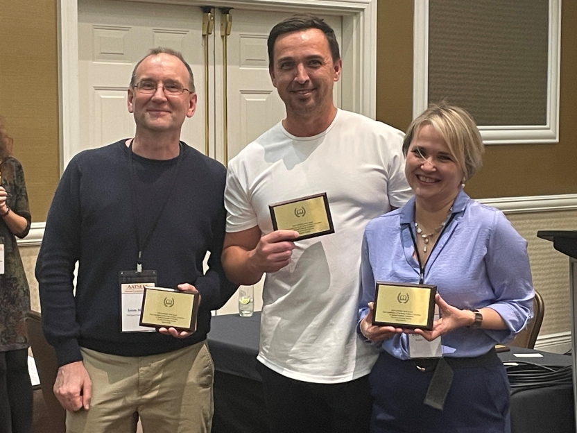 Three people stand with their awards, smiling at the camera