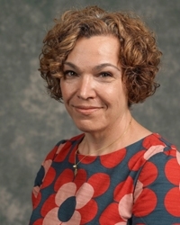 A woman in a patterned shirt smiles at the camera.