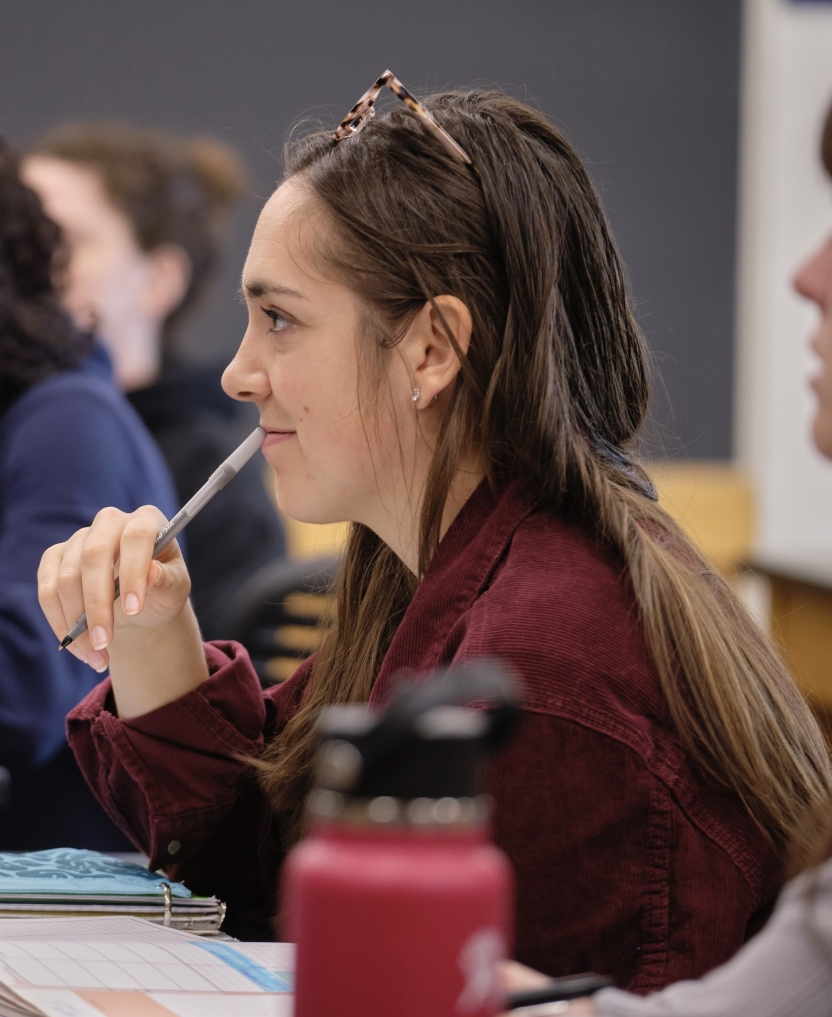 A student thinks with her pen to her mouth in class.