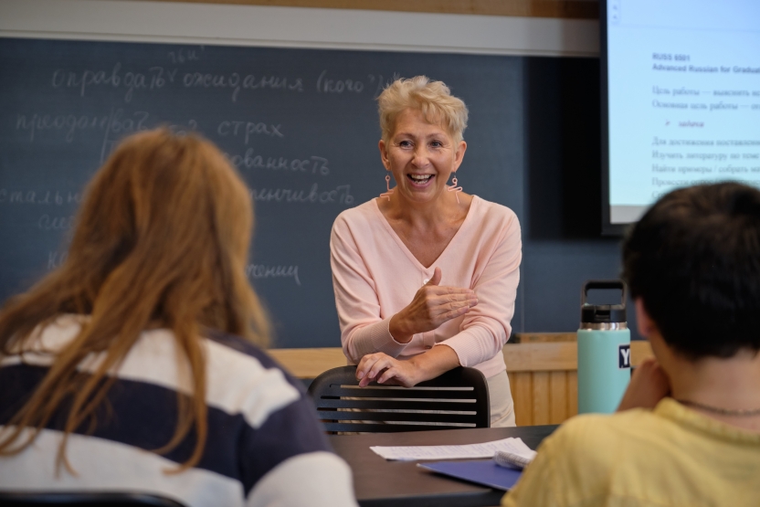 A teacher speaks with her students in front of a white board, smiling.
