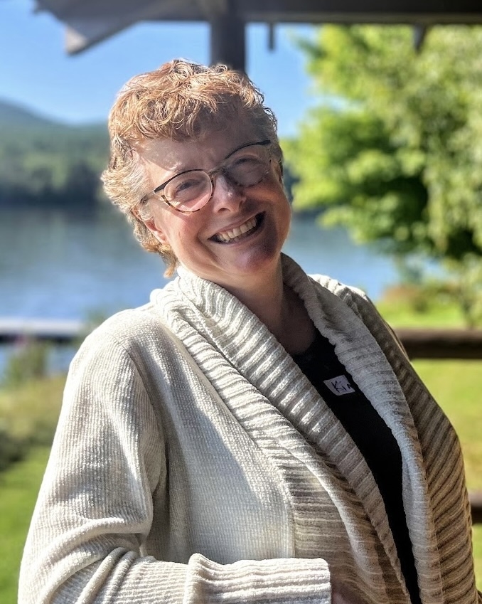 A woman smiles at the camera in front of a lake.