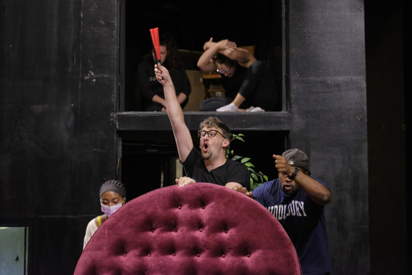 A student raises his hand, acting in a play. 