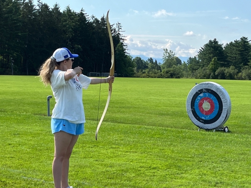 A student practices archery on a lawn. 