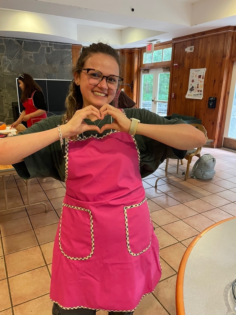 A student in a pink apron makes a heart with her hands