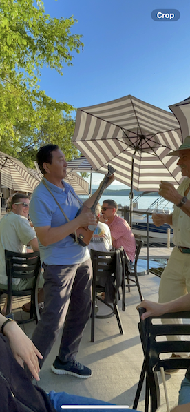 A man plays an instrument outside under an umbrella. 