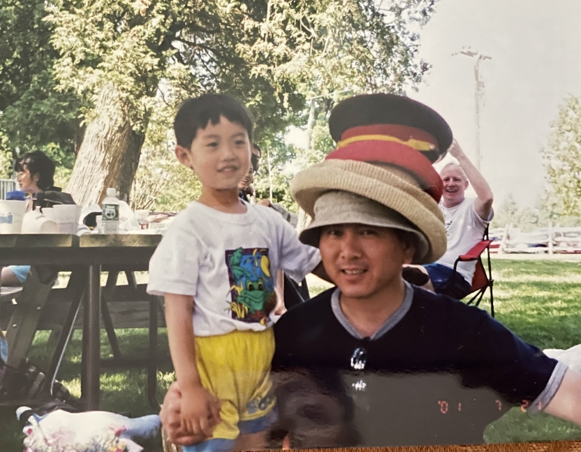 A man wears many hats, posing with his son. 