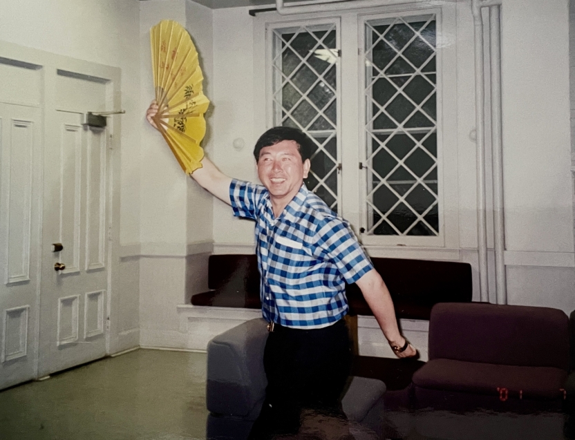A man with a fan poses and smiles at the camera. 